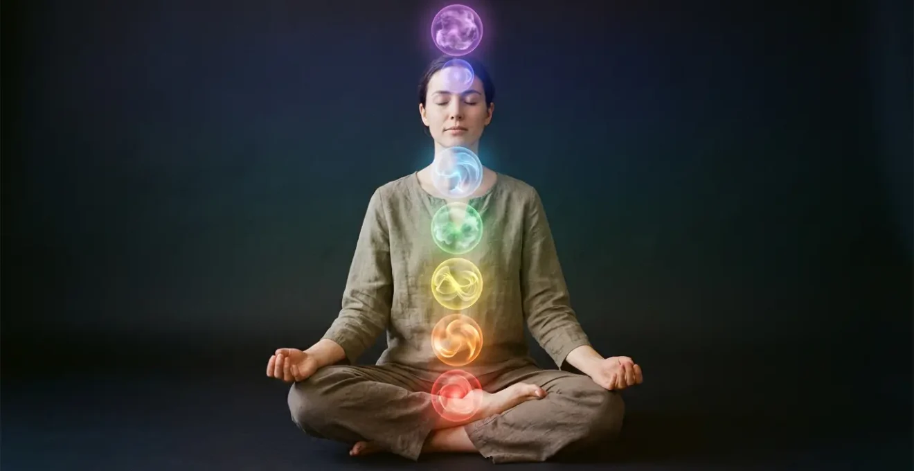 Persona en posición de meditación con representación simbólica de los siete chakras a través de luces de colores que fluyen por el cuerpo