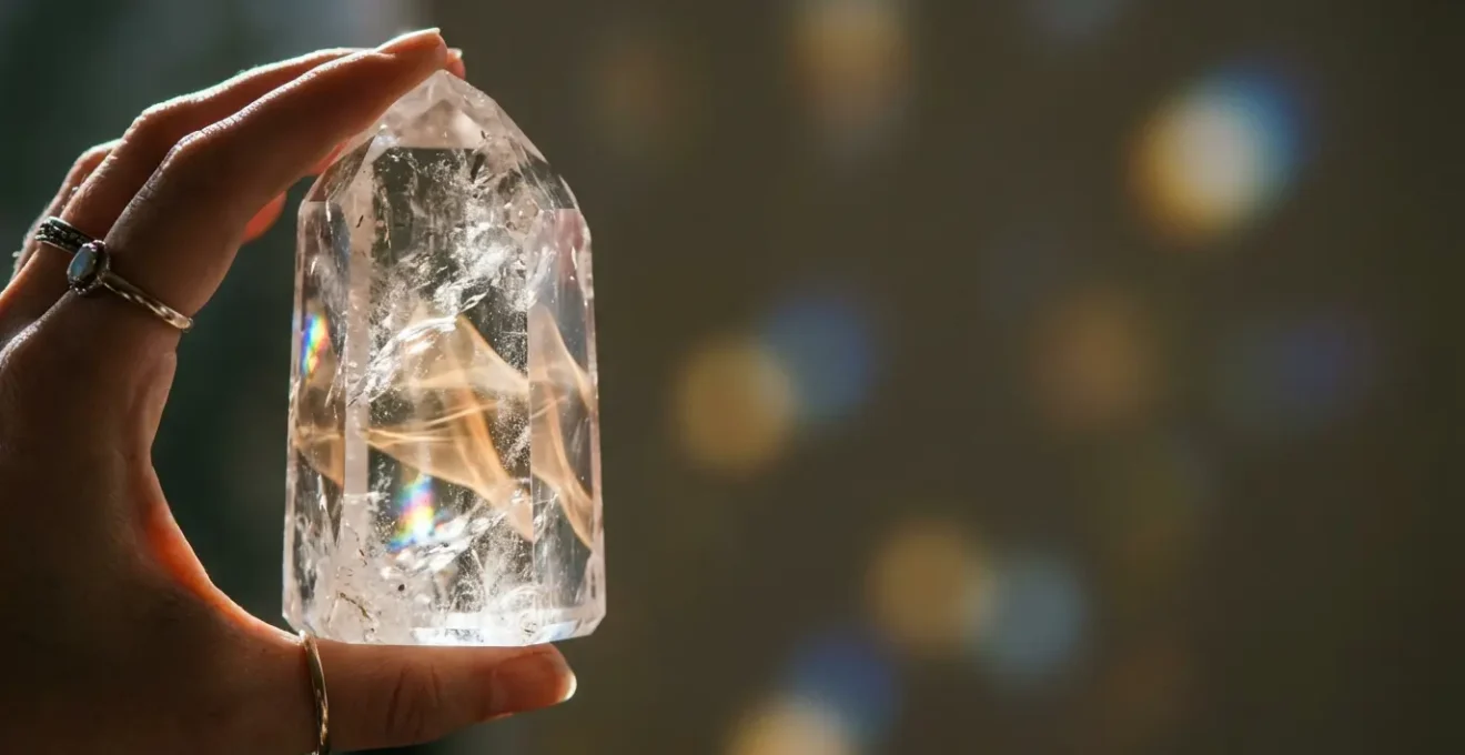 Cristal de cuarzo transparente en mano siendo programado con luz dorada y energía vibratoria para manifestar intenciones