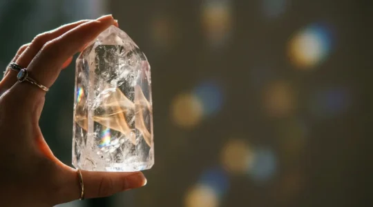 Cristal de cuarzo transparente en mano siendo programado con luz dorada y energía vibratoria para manifestar intenciones